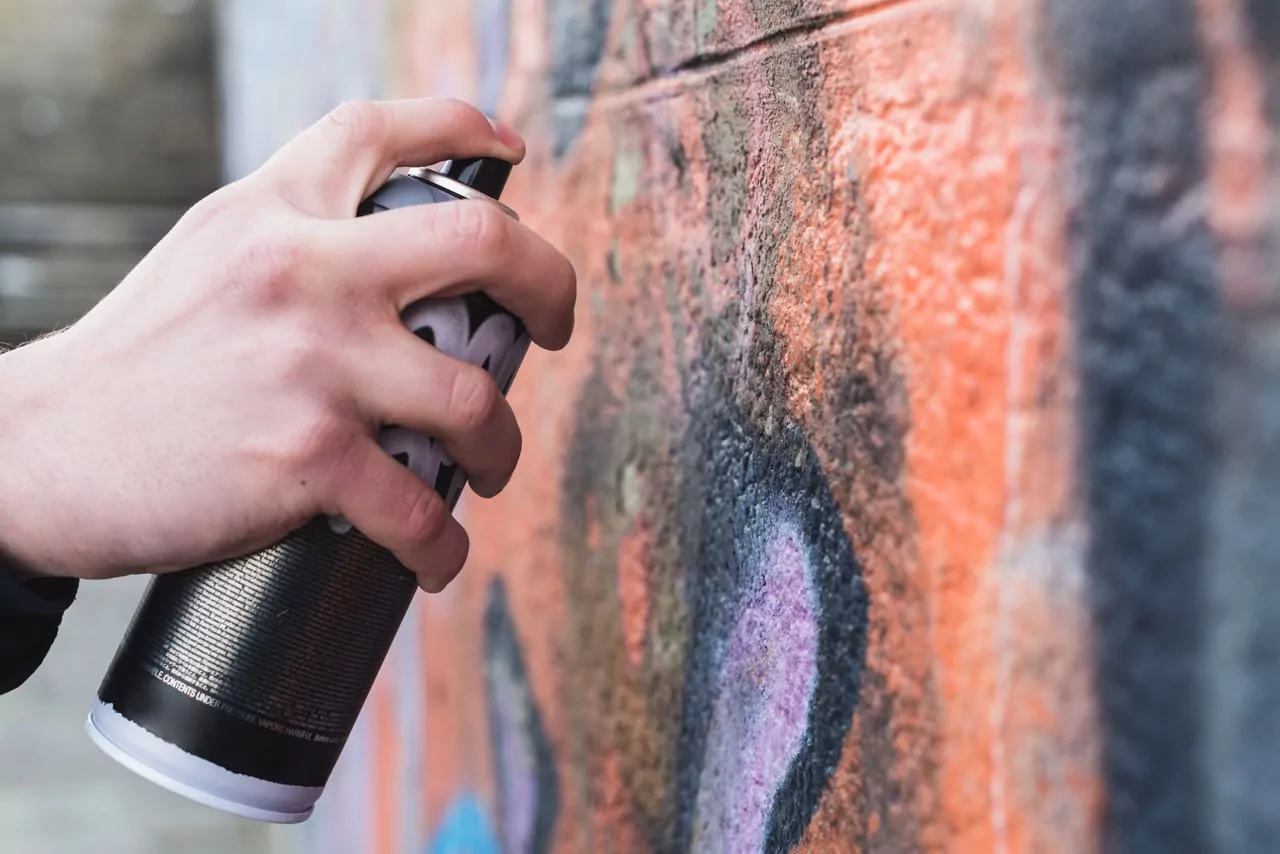 Hand mit Sprühdose vor einer besprühten Wand, passend zum Thema Graffiti entfernen.