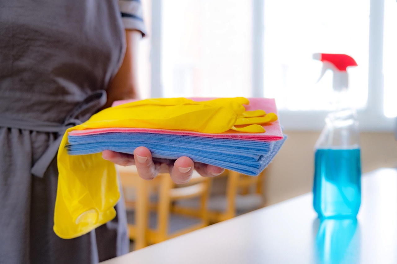 Person hält Putztücher und gelbe Handschuhe in der Hand, daneben steht eine Sprühflasche für die Unterhaltsreinigung.