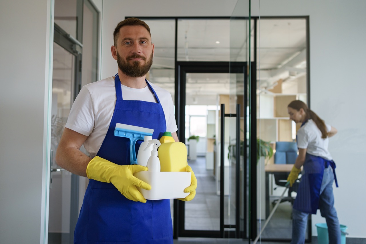 Reinigungskraft mit Reinigungsmitteln in einem Büro, passend zum Thema Gebäudereinigung Kosten.