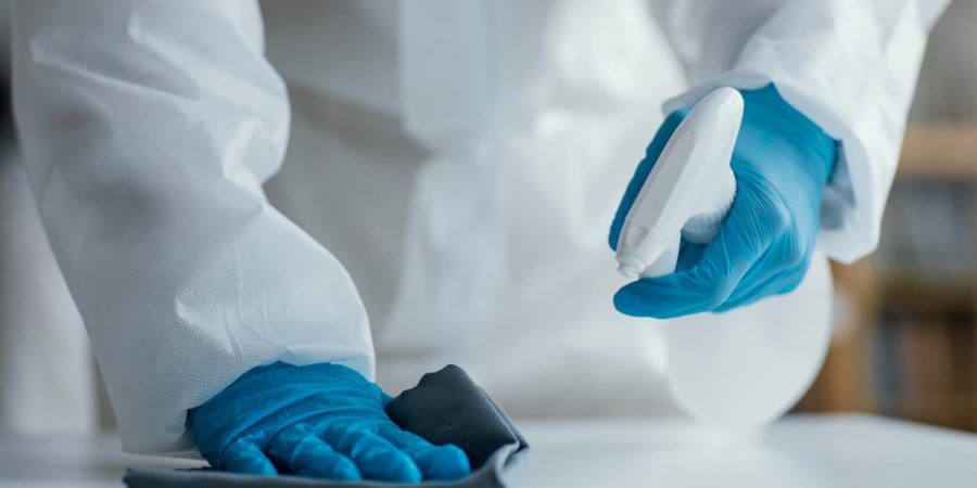 Reinigungskraft mit blauen Schutzhandschuhen beim HACCP Reinigen einer Oberfläche mit Tuch und Sprühflasche.