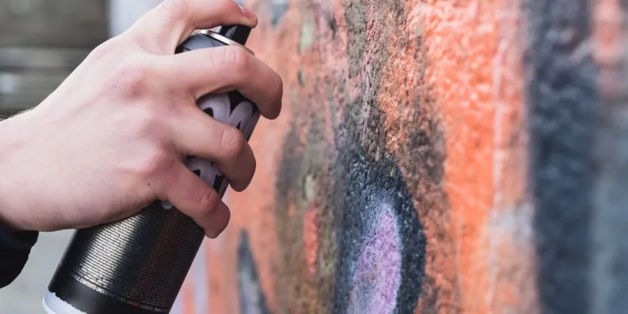 Hand mit Sprühdose vor einer besprühten Wand, passend zum Thema Graffiti entfernen.