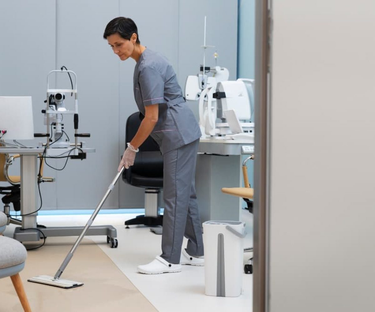 Reinigung von Arztpraxen mit Wischmopp in einem Behandlungsraum mit medizinischen Geräten