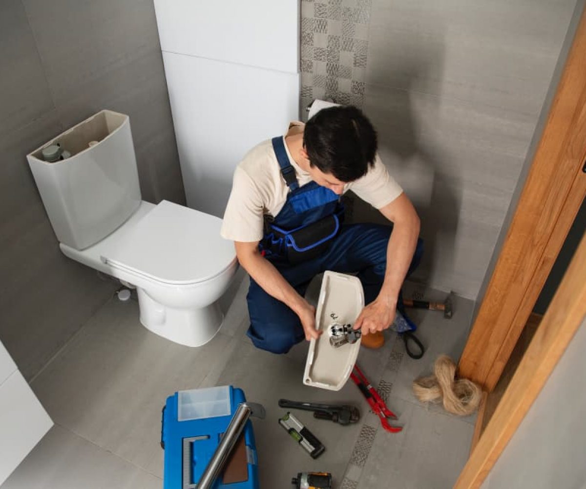 Hausmeisterdienste mit Reparaturarbeiten an einer Toilette durch einen Mitarbeiter mit Werkzeug