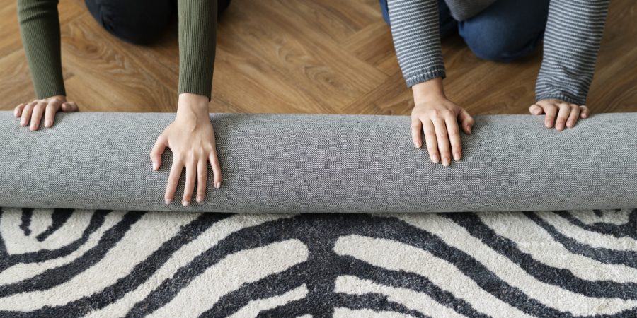 Zwei Personen rollen einen Teppich in einer Wohnung auf, passend zum Thema Motten im Teppich.