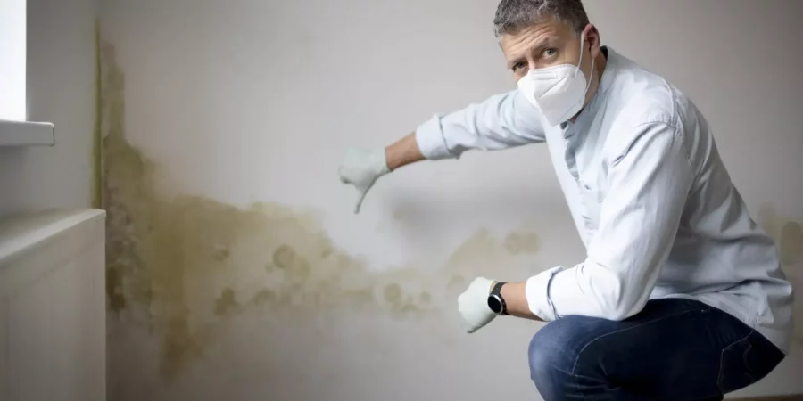 Mann mit Atemschutz behandelt eine Wand, Vorbeugen gegen Schimmel in der Wohnung