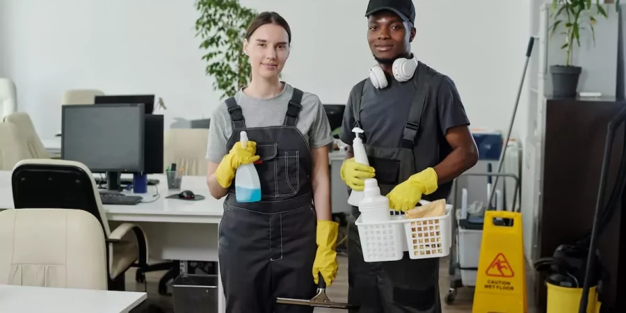 Zwei Reinigungskräfte stehen mit Sprühflaschen und Reinigungszubehör in einem Büro eines Reinigungsunternehmens Karlsruhe.