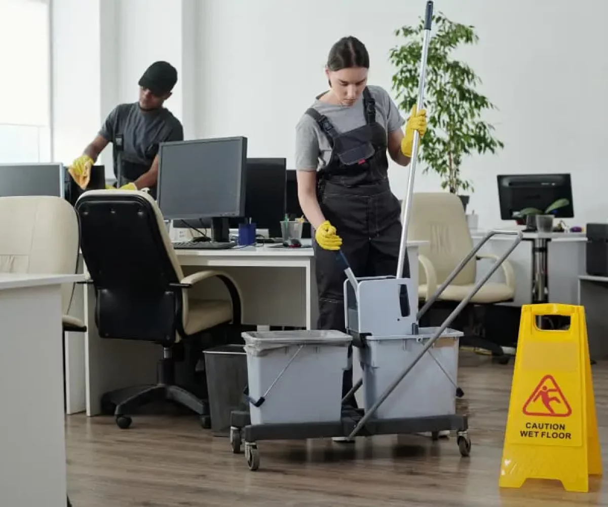 Unterhaltsreinigung in einem Büro mit Reinigungsteam, Wischwagen und Warnschild für nasse Böden